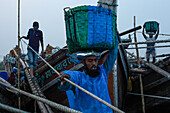 Chittagong, Bangladesh - 28 November 2019: View of fishermen hauling vibrant blue and green baskets ashore near the bustling docks, a scene of tireless labor and maritime tradition.