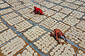 Bogura, Bangladesh - 16 May 2020: Aerial view of women in vibrant saris spread across meticulously arranged mats covered with sun-drying Papadums, creating a mesmerizing geometric pattern.