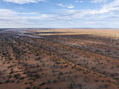 Luftaufnahme der ausgedehnten und trockenen Kalahari-Wüstenlandschaft unter einem heiteren Himmel mit vereinzelten Wolken, Hardap, Namibia.