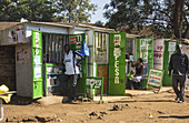 Kisumu, Kenya - 13 May 2021: View of vibrant green M-PESA kiosks line a dusty street, bustling with activity under the warm Kenyan sun.