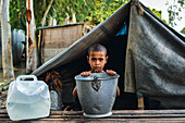 Bogura, Bangladesh - 04 August 2015: View of a young boy standing in front of a makeshift tent, a poignant scene of resilience amid humble surroundings.