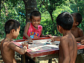 Mirsharai, Bangladesch - 21. Oktober 2019: Blick auf Kinder, die sich um ein Carrom-Brett versammelt haben, ihre Gesichter strahlen vor Freude inmitten des üppigen Grüns.