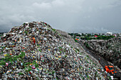 Chattogram, Bangladesch - 05. Oktober 2020: Blick auf ein Kind, das auf einem riesigen Berg weggeworfenen Mülls steht, der sich von der entfernten Stadtlandschaft abhebt.