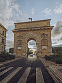 View of an ancient triumphal arch stands proudly against the sky, the French flag fluttering atop, with zebra crossing offering passage, Montpellier, Occitanie, France.