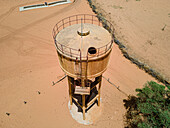 Aerial view of a faded water tower standing tall against the arid landscape, its metal reflecting the harsh sunlight, Khol Khol, Louga Region, Senegal.