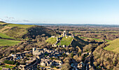 Luftaufnahme der verwitterten Steinmauern von Corfe Castle, das stolz auf einem Hügel steht und das malerische Dorf darunter überblickt, Dorset, Vereinigtes Königreich.