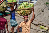 Dhaka, Bangladesh - 08 April 2023: View of a man carrying a basket full of vibrant green watermelons on his head, a testament to the bustling trade in the city's heart.