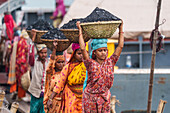 Dhaka, Bangladesh - 14 May 2023: View of women balancing baskets laden with dark coal on their heads, a vivid display of labor against the backdrop of the city's bustling port.