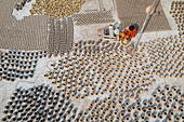 Bogura, Bangladesh - 22 October 2019: Aerial view of countless pots drying under the sun, creating a textured landscape of earthy tones, as a person in vibrant attire moves amongst them.