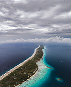 Luftaufnahme eines schmalen Landstreifens, der den tiefblauen Ozean von der türkisfarbenen Lagune trennt, unter einem bewölkten Himmel, Fakarava, Iles Tuamotu-Gambier, Französisch-Polynesien.
