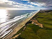 Luftaufnahme des langen Sandstrandes, an dem der türkisfarbene Ozean auf üppig grünes Land trifft, unter einem bewölkten Himmel, Dargaville, Region Northland, Neuseeland.