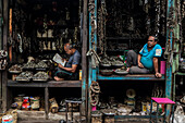 Dhaka, Bangladesh - 09 November 2019: View of two men in adjacent shops surrounded by an abundance of metal items, creating a scene of concentrated commerce.