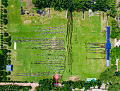 Bogura, Bangladesh - 07 March 2019: Aerial view of a vast green field dotted with orderly lines of people, framed by the deep shadows of trees, creating a striking contrast.