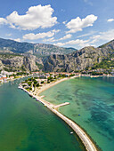 Luftaufnahme des Flusses Cetina, der in die Adria mündet, geteilt durch einen Sandstrand und einen felsigen Wellenbrecher, unter hoch aufragenden Klippen, Omis, Gespanschaft Split-Dalmatien, Kroatien.