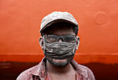 Dhaka, Bangladesh - 25 October 2019: View of a man covered in dust, his eyes peering through smudged glasses, against a stark orange backdrop, a gritty portrait of labor in Dhaka.