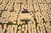 Bogura, Bangladesh - 30 July 2025: Aerial view of a man smiling brightly amidst a sea of drying food, creating a textured landscape of light and shadow.