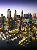 Perth, Australia - 08 June 2025: Aerial view of the Esplanade waterfront glows with vibrant lights against the twilight sky, reflecting off the dark waters and modern cityscape backdrop.