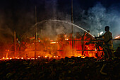 Narayanganj, Bangladesh - 07 November 2020: View of a dramatic scene unfolds as water arcs against the night sky, dousing the burning pyre amidst silhouettes of solemn onlookers.