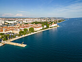 Luftaufnahme von leuchtend orangefarbenen Dächern, die in die tiefblaue Adria entlang der historischen Stadtküste von Zadar, Kroatien, übergehen.