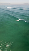 Aerial view of a lone surfer carving through the turquoise waters, with distant mountains fading into the misty horizon, Cape Town, Western Cape, South Africa.