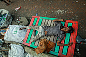 Dhaka, Bangladesh - 15 August 2021: View of a smiling boy lies on a vividly painted wooden pallet amidst the stark reality of waste and poverty.