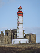 View of the striking Phare Saint-Mathieu lighthouse standing tall beside ancient stone ruins against a serene blue sky, Plougonvelin, Bretagne, France.