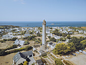 Aerial view of the stark white Trezien lighthouse piercing the skyline amidst a quaint village, overlooking the azure sea, Plouarzel, Bretagne, France.
