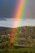 Aerial view of a vivid rainbow stretches across the sky, its radiant colors contrasting sharply against the dark clouds above the lush green hills, Poniky, Banskobystrický kraj, Slovakia.