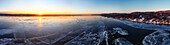Aerial view of a frozen river reflecting the vibrant sunset, with ice sheets and distant bridge contrasting against the shoreline, Nyack, New York, United States.