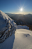 View of a sunburst over a snow-laden mountain peak, casting shadows on the soft, undulating snowscape in Velka Fatra mountains, Majerova skala rock, Staré Hory, Banskobystrický kraj, Slovakia.