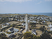 Aerial view of the stark white Phare de Trezien lighthouse standing tall amidst the village homes against the blue of the sea, Plouarzel, Bretagne, France.
