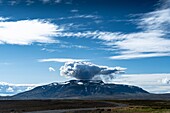 Blick auf einen dramatischen, grüblerischen Berg, der von einer wirbelnden Wolke unter einem weiten Himmel gekrönt wird, im Kontrast zur ruhigen Landschaft, Blafell, Bláskógabyggð, Island.