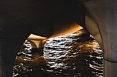 View of shimmering water reflecting golden light beneath the concrete arches, a stark contrast of textures and tones, creating a mesmerizing scene, New York, New York, United States.