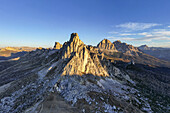 Luftaufnahme von zerklüfteten Gipfeln, die vom Sonnenlicht geküsst werden und lange Schatten auf das felsige Gelände des Passo Giau werfen, Cortina d'Ampezzo, Belluno, Italien.