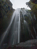 View of ethereal waterfall cascades down moss-covered cliffs, a serene spectacle of nature's power and beauty, creating a tranquil oasis, Vik, Iceland.