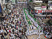 Chattogram, Bangladesh - 16 September 2024: Aerial view of a vibrant street filled with a multitude of people marching, waving green flags amidst aged buildings.