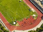 Aerial view of a vibrant green sports field meeting a red running track, with people scattered across the space, Perugia, Umbria, Italy.