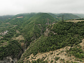 Luftaufnahme einer tiefen Schlucht, die sich unter bewölktem Himmel durch üppig grüne Berge zieht, Tatev, Provinz Syunik, Armenien.