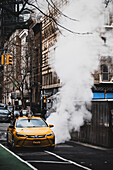 New York, United States - 24 December 2023: View of a vivid yellow taxi contrasts against the gritty urban backdrop, steam billowing into the cold air near historic buildings.