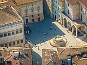 Aerial view of a bustling square features the Fontana Maggiore as people stroll across the stone pavement, surrounded by buildings with terracotta roofs, Perugia, Umbria, Italy.