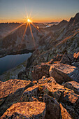 Aerial view of the sun bursting over the rugged peaks and still waters of a lake, casting long shadows, Vysoké Tatry, Prešov Region, Slovakia.