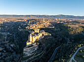 Aerial view of the Alcázar of Segovia rising majestically above the landscape, bathed in golden light, with the city sprawling in the background, Segovia, Castilla y León, Spain.