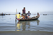 Cox's Bazar, Bangladesh - 29 November 2022: View of local boys clustered on a traditional wooden boat, its reflection shimmering on the tranquil waters, under a clear, expansive sky.