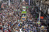 Chattogram, Bangladesh - 16 September 2024: Aerial view of a vibrant, dense crowd filling the street, a sea of faces and green flags surrounding decorated vehicles.
