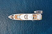 Aerial view of a luxurious yacht, gleaming white against the deep azure sea, with a smaller boat alongside, reflecting the summer sun, Sicily, Italy.