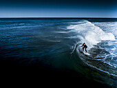 Aerial view of a surfer riding a powerful, curling wave, the deep blue sea contrasting with the white foam, Gracetown, Western Australia, Australia.