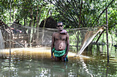 Noakhali, Bangladesh - 02 September 2024: View of a fisherman standing waist-deep in murky floodwaters near a fishing net, amidst lush green foliage.