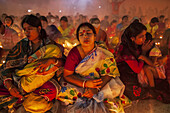 Narayanganj, Bangladesh - 15 November 2022: View of women in colorful saris, heads bowed in solemn prayer, illuminated by the soft glow of candles.