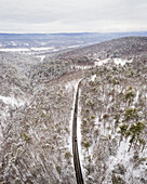Aerial view of a ribbon of asphalt cutting through a frosted forest, the snow-laden trees casting long shadows under a soft, diffused light, Fawn Lake Forest, Pennsylvania, United States.