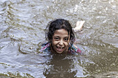 Noakhali, Bangladesh - 02 September 2024: View of a girl's bright smile cuts through the murky water, a moment of pure joy captured in the river's embrace.
